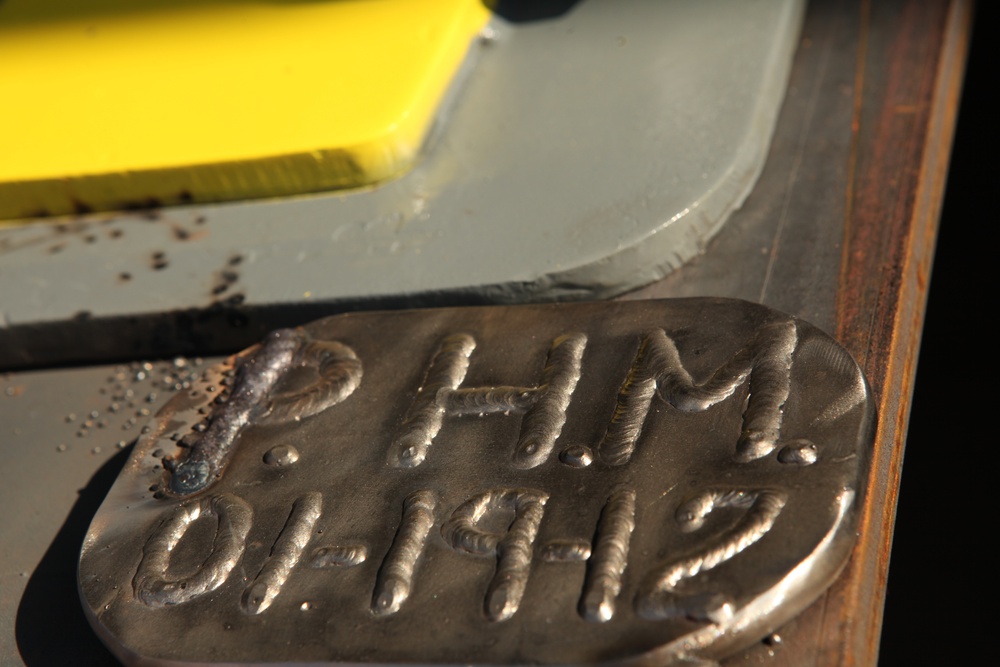 Honorary guest Pat Mills brands her initials into the metal of Department of the Navy's newest Mobile Landing Platform