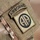 Close-up photograph of a U.S. Army uniform sleeve displaying the 82nd Airborne Division shoulder sleeve insignia. The patch features the distinctive 'AA' (All American) double-A emblem within a circular design, accompanied by an 'AIRBORNE' tab above it. The uniform is MultiCam (OCP) camouflage pattern.