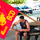 A young muscular man in a navy blue sleeveless shirt sits at an outdoor picnic table holding a large red Marine Corps flag. The flag displays 'MC BCD MB WASH DC' in yellow lettering along with the Eagle, Globe, and Anchor emblem. The setting appears to be a military base or outdoor recreational area with vehicles and trees visible in the background.