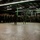 From cold to freezing, Marines head to the Arctic Circle A large group of military personnel in camouflage uniforms are assembled in a semicircle inside a large industrial warehouse or hangar facility. Two individuals appear to be addressing or briefing the assembled troops from the center of the formation. The setting suggests a pre-mission briefing, unit assembly, or training exercise.