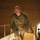 From cold to freezing, Marines head to the Arctic Circle A male military service member in U.S. Marine Corps MARPAT (digital camouflage) uniform is descending a metal diamond-plate staircase in what appears to be an indoor facility or bunker. He is wearing tan/desert combat boots and has rank insignia visible on his collar. The lighting is warm and directional, coming from below the staircase.
