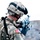 Big Island Military Police Training March 23-24 A U.S. Army soldier in full combat gear is actively firing a weapon, with spent brass casings visibly ejecting from the firearm. The soldier is wearing Army Combat Uniform (ACU) in Universal Camouflage Pattern (UCP) with an American flag patch on the left shoulder. The setting appears to be an outdoor training or operational environment with rocky terrain in the background.