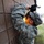 A U.S. Air Force Airman in ABU (Airman Battle Uniform) is performing maintenance work on an exterior wall-mounted light fixture of a building. The service member is reaching up into the fixture housing, appearing to replace or inspect a light bulb while wearing black tactical gloves. The rank insignia visible on the sleeve indicates the rank of Airman First Class.