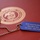 The image shows a blue military-style dog tag on a ball chain necklace resting on a red folder or document cover embossed with the United States Marine Corps seal. The dog tag is engraved with gold text reading 'MCAS Camp Pendleton, Mary Munn Day, NO FUSS - JUST FUN.' This appears to be a commemorative or event souvenir item associated with Marine Corps Air Station Camp Pendleton.