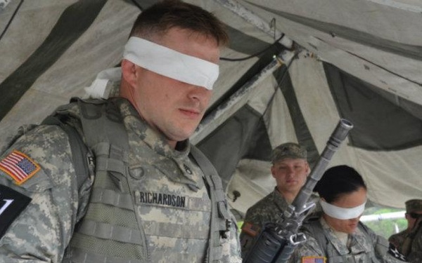 Multiple U.S. Army soldiers in ACU (Army Combat Uniform) are performing a blindfolded weapons handling exercise under a military tent. The soldiers are wearing white blindfolds and are handling M16/M4 rifles, likely practicing blind assembly or disassembly. Each soldier is numbered sequentially (41, 44, 43 visible), suggesting a competitive or evaluated training event.