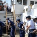 Coast Guardsmen, including Coast Guard Academy cadets work as a team heaving a line to hoist the main sail aboard Coast Guard Barque Eagle