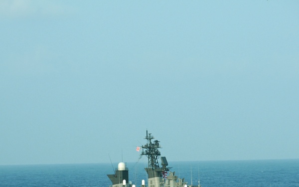 A gray naval warship bearing hull number '144' is underway on open blue ocean waters. A flag consistent with the Japanese Maritime Self-Defense Force (JMSDF) ensign is visible on the mast. The vessel appears to be a destroyer-class warship equipped with various radar and weapons systems.
