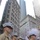 A formation of U.S. Marines in Service Charlie (khaki shirt, blue trousers with red stripe) uniforms stands at attention during a ticker-tape parade in a dense urban canyon, likely New York City. Red, white, and blue confetti fills the air around tall commercial buildings. Navy personnel in white uniforms are also visible in the background.
