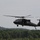 Patriot Exercise 2012 A military helicopter, consistent with a UH-60 Black Hawk, is captured in low-altitude flight against an overcast sky. The aircraft is painted in olive drab/dark green military livery and appears to be either taking off or landing near a treeline. The main rotor blades show motion blur indicating active flight.