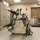 The image shows an indoor storage or equipment room containing a wheeled cart or rack holding multiple cylindrical tool-like devices, possibly torque wrenches or pneumatic tools. The room features gray metal storage cabinets, a fire alarm pull station, and an exit door with push-bar hardware. The setting appears to be a maintenance, industrial, or institutional facility.