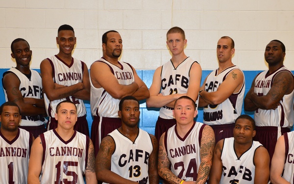 A basketball team photo taken inside a gymnasium, featuring approximately 14 players arranged in two rows. The team appears to represent Cannon Air Force Base (CAFB), with players wearing white and maroon jerseys labeled 'CANNON' or 'CAFB'. A Wilson Evolution basketball is placed on the floor in front of the group.