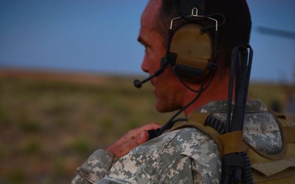 A U.S. Army soldier is photographed from behind/side in an outdoor arid environment. The soldier is wearing ACU (Army Combat Uniform) digital camouflage pattern and is equipped with tactical gear including a plate carrier, assault pack, and communications headset. Patches on the pack identify the soldier as belonging to Special Forces and Airborne units.