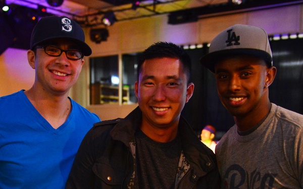 Three young men are posing together for a photo in what appears to be a bar or entertainment venue. The man in the center is holding up a CD or album with 'Full Service' visible on the cover and giving a thumbs up. The group appears to be in good spirits at what may be a music-related event.