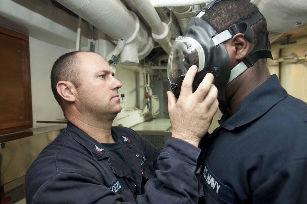 USS Hue City sailor helps another with gas mask