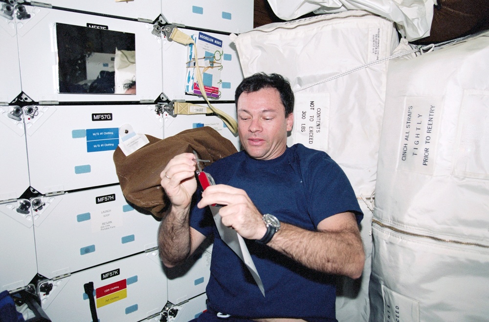 Wakata and McArthur prepare a meal; Lopez-Alegria with a Swiss knife
