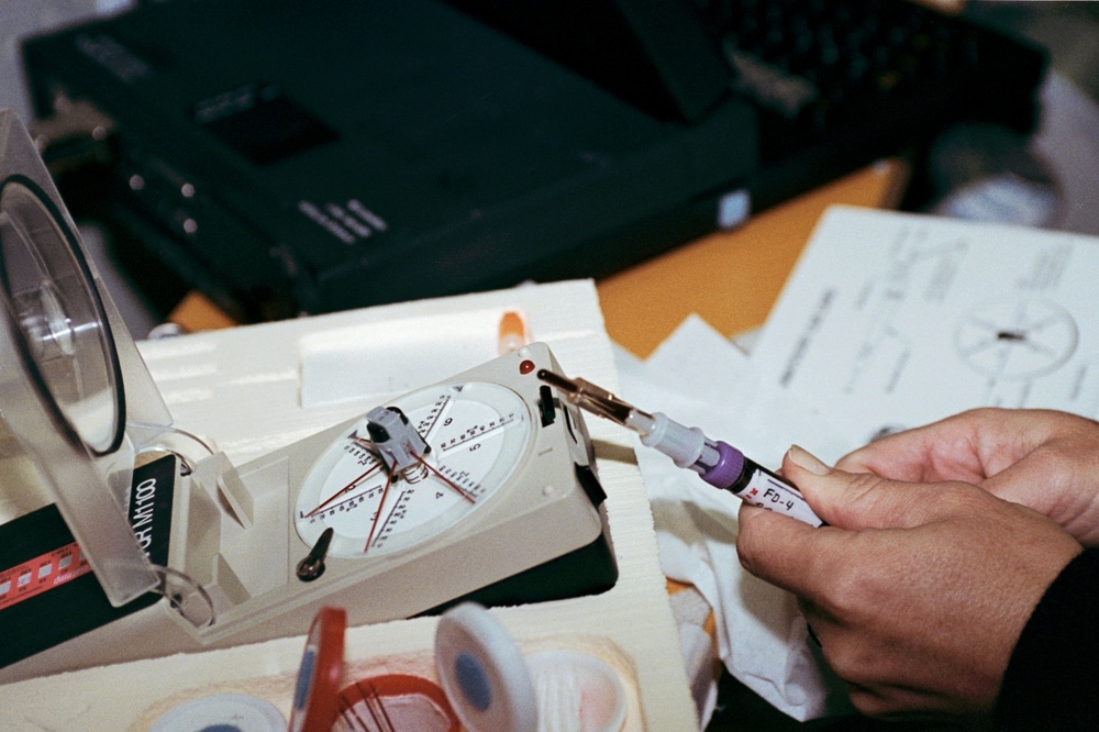 Crewmember in SPACELAB preparing blood samples for processing in centrifuge.