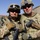 Two Kentucky soldiers embrace for a photo together in southern Afghanistan Two U.S. Army soldiers in full combat gear pose together for a photo, likely at a forward operating base in a desert environment. Both wear MultiCam (OCP) uniforms, tactical helmets with mounted optics, and are armed. Name tapes and unit patches are partially visible on their uniforms.