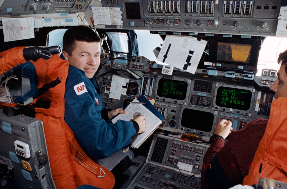 Crewmembers in the fwd flight deck reviewing inflight procedures manual.