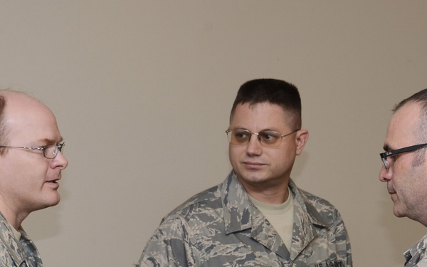 Three military personnel in U.S. Air Force Airman Battle Uniform (ABU) digital camouflage are engaged in what appears to be an interview or discussion. The person on the right is holding a small recording device or smartphone toward the person on the left, suggesting a media or documentation activity. All three individuals wear glasses and display visible rank insignia on their sleeves.