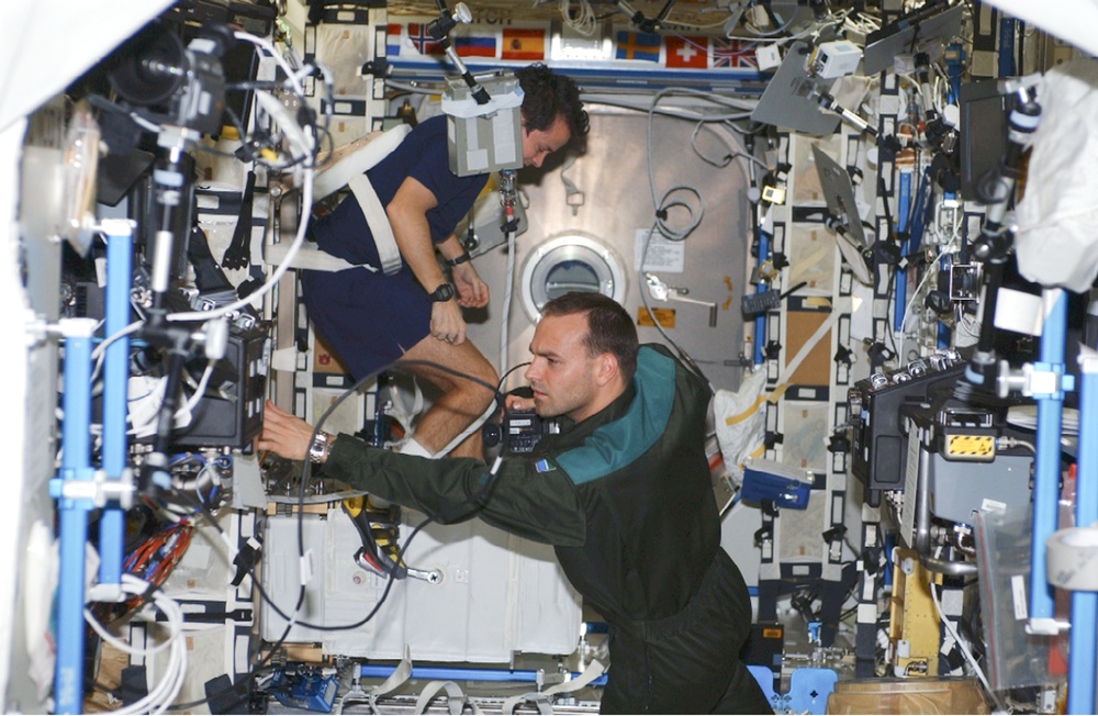 Shuttleworth works in U.S. Lab as Bursch exercises on cycle Ergometer during Expedition Four