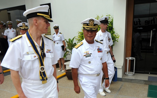 A group of naval officers in white dress uniforms are walking together outside what appears to be an official building or conference venue. The officers appear to represent multiple nations, suggested by the varying cap insignia and medal ribbons visible on their uniforms. The scene suggests a formal military meeting, ceremony, or diplomatic event.