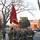 A formation of U.S. Marines in physical training (PT) gear conducting a unit run along a road on what appears to be a military installation. The lead Marine carries a red U.S. Marine Corps guidon flag with gold fringe. The Marines are in uniform wearing MARPAT camouflage trousers, olive drab sweatshirts, and high-visibility yellow/green safety belts.