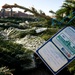 The image shows bundled Christmas trees tagged with 'Trees for Troops' program cards, a charitable initiative that ships real Christmas trees to deployed military personnel. A handwritten note is visible on the tag expressing holiday wishes and gratitude to service members. Military personnel in uniform are visible in the blurred background.