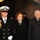 57th Presidential Inauguration Three individuals are pictured in what appears to be a formal indoor setting with ornate lighting visible in the background. A young naval officer in dress uniform with gold aiguillette is escorting an elderly woman and an elderly man, all dressed in dark formal attire. The setting and attire suggest a significant ceremonial or official event.