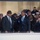 National Guardsmen support 57th Presidential Inaugural Parade Two men in dark suits and ties are standing in what appears to be an enclosed viewing box or VIP area, sharing a friendly interaction with one placing his hand on the other's shoulder. They are surrounded by a large crowd of seated and standing attendees, including individuals in military uniforms, suggesting a formal public event. The setting appears to be an official ceremony or parade, indicated by the formal attire and organized seating arrangement.