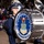 United States Air Force Band passes presidential reviewing stand A member of The United States Air Force Band marches in a parade in Washington D.C., carrying a large bass drum prominently displaying the USAF Band seal and insignia. The drummer is dressed in the formal dark blue Air Force dress uniform with a white peaked cap. A crowd of spectators is visible in the background, suggesting a formal military parade or ceremonial event.