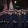 National Guardsmen support 57th Presidential Inaugural Parade A large military formation is marching in what appears to be a formal parade, likely in Washington D.C. based on the street setting and signage. The personnel are wearing dark navy dress overcoats with gold buttons and white peaked caps, consistent with U.S. Coast Guard or Navy dress uniforms. Color guard members carrying an American flag and unit guidons are visible in the background.