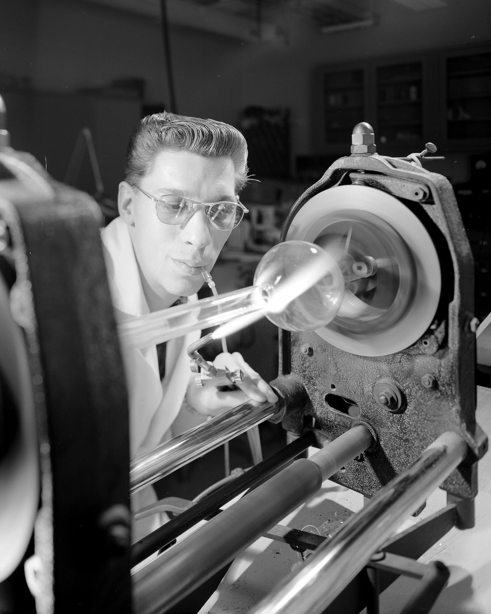 TOM SEITZ SCIENTIFIC GLASS BLOWER AT GLASS FABRICATION LABORATORY SHOWN CREATING CUSTOM GLASSWARE FOR CHEMICAL PHYSICAL RESEARCH