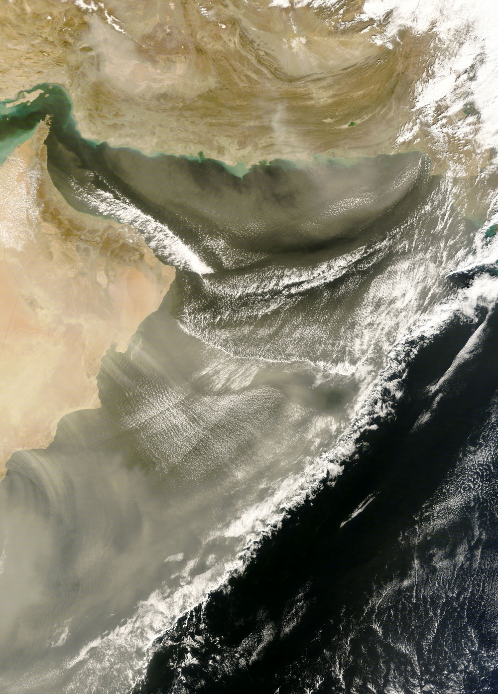 This is a satellite image showing a large dust storm (haboob) originating from the Arabian Peninsula and sweeping across the Arabian Sea and Gulf of Oman. The dust plume extends from the arid desert landmass in the upper-left and lower-left portions of the image, moving southeastward over the dark ocean waters. The Persian Gulf is visible in the upper portion of the image, with the Strait of Hormuz and Oman coastline identifiable.