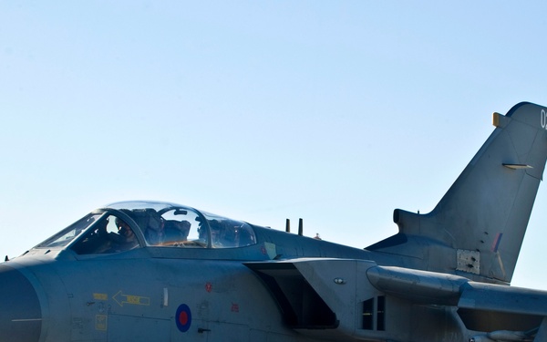 A Royal Air Force Panavia Tornado GR4 jet aircraft, serial number 022, is taxiing or parked on an airfield tarmac. The aircraft displays the RAF roundel (red, white, and blue concentric circles) on its fuselage and is equipped with external fuel tanks and underwing stores. Ground crew personnel and support vehicles are visible in the background.