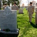 Four U.S. Navy personnel in service khaki uniforms are gathered at the grave of Delbert D. Black at what appears to be Arlington National Cemetery. The headstone identifies him as GMCM U.S. Navy, the First Master Chief Petty Officer of the Navy, a Pearl Harbor Survivor who lived from July 11, 1922 to March 5, 2000. A red rose has been placed at the base of the headstone as a tribute.