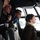 Several young people are inside what appears to be the cockpit or flight deck of a large vintage or military aircraft. One individual is holding a radio handset/microphone while others look out through the large curved cockpit windows. The setting suggests a tour or open-day visit to a historic aircraft.