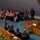 Hawaii State Medal of Honor ceremony pays tribute to fallen service members A formal ceremony or official government session is taking place in what appears to be a legislative chamber or auditorium. An elderly man in a suit is speaking at a wooden podium/lectern while an audience of dignitaries, officials, and guests — many wearing Hawaiian lei garlands — are seated in rows. Military personnel in uniform are also present among the attendees.
