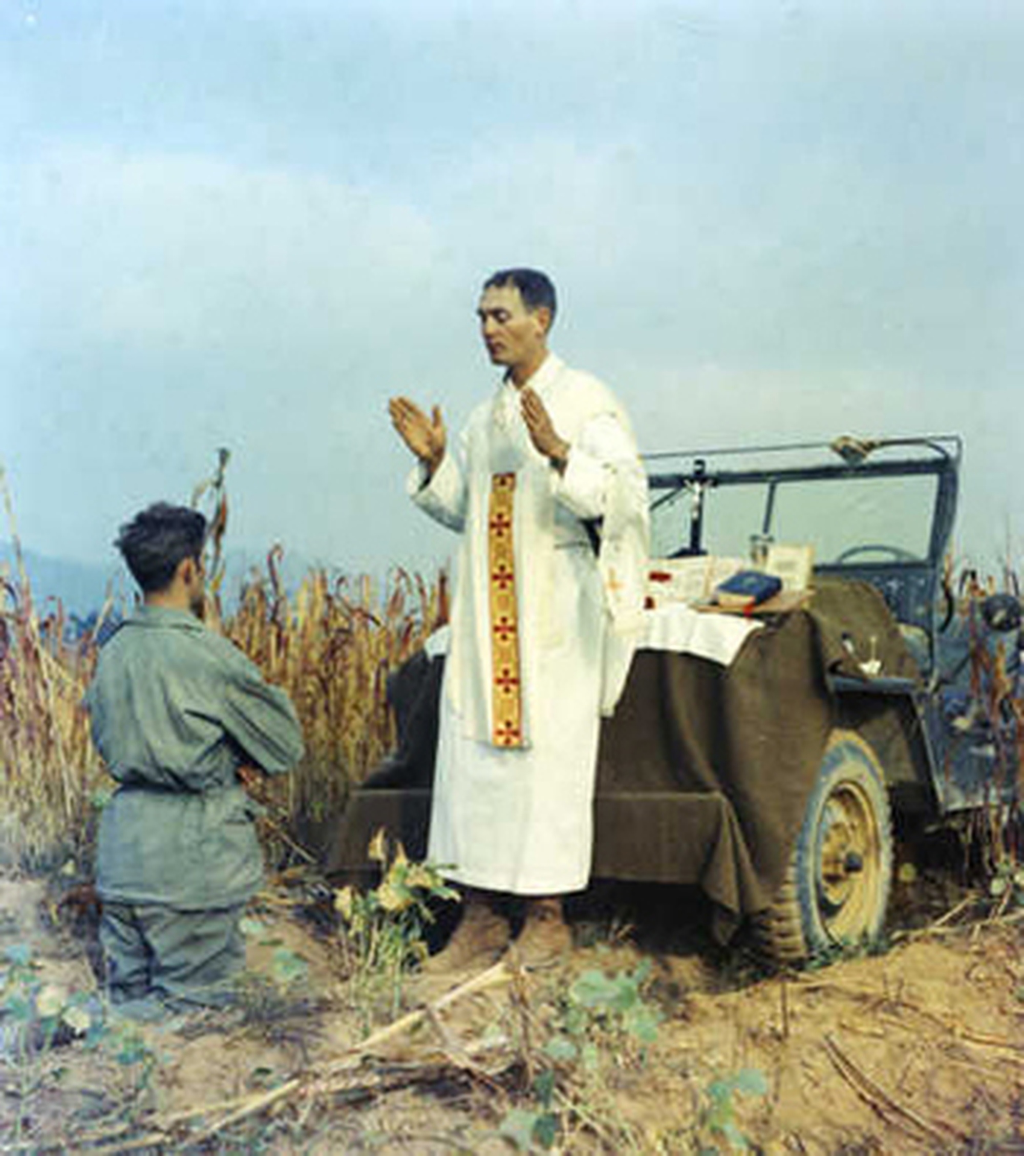 Father Emil Kapaun celebrating Mass on the hood of a Jeep, with a kneeling soldier in the foreground
