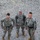 Region 3 Best Warrior Competition Three U.S. Army soldiers in Army Combat Uniform (ACU) pattern are photographed from an elevated angle, standing on a gravel surface near a wooden beam or barrier. The soldiers are equipped with rappelling/climbing gear including carabiners and harnesses. The leftmost soldier's name tape reads 'LACROSSE' and all three wear U.S. Army insignia with shoulder patches.