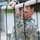 Region 3 Best Warrior Competition A U.S. Army soldier in Army Combat Uniform (ACU) digital camouflage pattern is gripping a rope or bar obstacle, appearing to be engaged in a physical training or obstacle course activity. The soldier displays a U.S. flag patch and what appears to be a unit patch on the left sleeve. The image is taken at close range with black ropes or cables visible in the foreground.