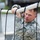 Region 3 Best Warrior Competition A U.S. Army soldier in Army Combat Uniform (ACU) digital camouflage pattern is navigating what appears to be a rope obstacle course or cargo net. He is gripping a white horizontal rope with both hands while black vertical ropes frame the foreground. The soldier displays focused determination and wears visible unit patches including a U.S. flag patch on his left shoulder.