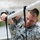 Region 3 Best Warrior Competition A U.S. Army soldier in Army Combat Uniform (ACU) is climbing or gripping a thick white rope while smiling. The soldier wears a reverse American flag patch on the right shoulder and an additional unit patch on the left sleeve. The image appears to be taken during a physical training or obstacle course exercise.
