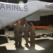 Military personnel are gathered on a flight line at night near a Marine Corps aircraft bearing the markings 'MARINES', 'VMM-264', and bureau number '166740'. Several individuals in various military uniforms appear to be engaged in conversation or a briefing near the aircraft. The setting appears to be a forward operating base or air station flight line.