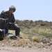 A U.S. Army soldier in ACU (Army Combat Uniform) is gathering and recovering parachute suspension lines after a landing in an arid, desert-scrub terrain. The soldier is kneeling and bundling the lines by hand, with the collapsed parachute canopy visible on the ground nearby. The setting appears to be a training or operational drop zone in a semi-arid environment.
