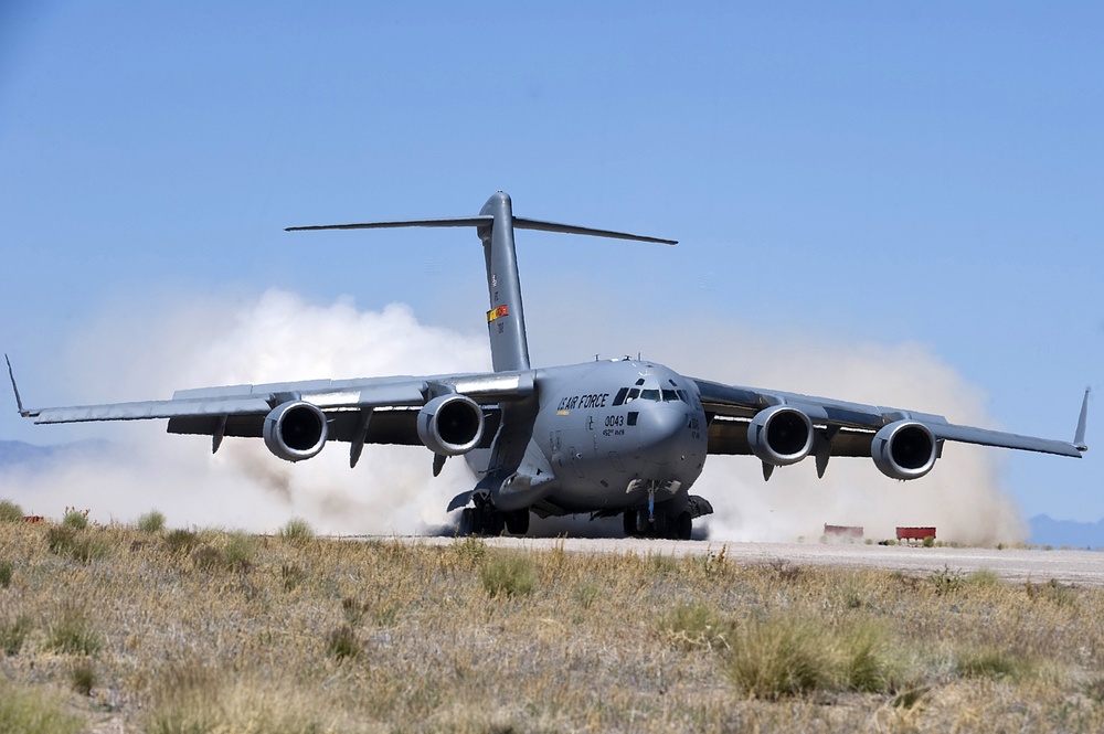 A U.S. Air Force C-17 Globemaster III military transport aircraft is operating on an unpaved or semi-prepared airstrip in an arid, desert-like environment. The aircraft bears the tail number 3043 and markings indicating it belongs to the 452nd Air Wing. Dust clouds are being kicked up behind the aircraft, suggesting it is either landing or performing a short-field takeoff/landing exercise.