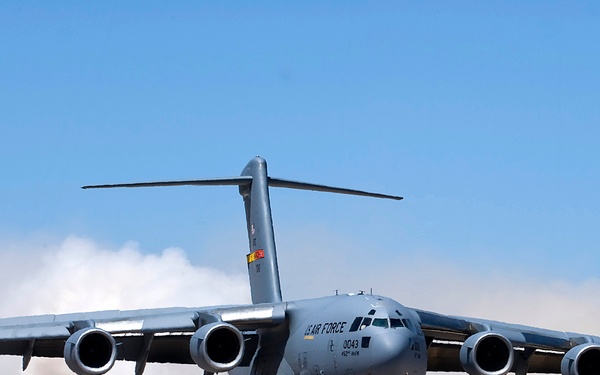 A U.S. Air Force C-17 Globemaster III military transport aircraft is operating on an unpaved or semi-prepared airstrip in an arid, desert-like environment. The aircraft bears the tail number 3043 and markings indicating it belongs to the 452nd Air Wing. Dust clouds are being kicked up behind the aircraft, suggesting it is either landing or performing a short-field takeoff/landing exercise.