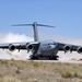 A U.S. Air Force C-17 Globemaster III military transport aircraft is operating on an unpaved or semi-prepared airstrip in an arid, desert-like environment. The aircraft bears the tail number 3043 and markings indicating it belongs to the 452nd Air Wing. Dust clouds are being kicked up behind the aircraft, suggesting it is either landing or performing a short-field takeoff/landing exercise.