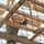 A soldier in military camouflage uniform is navigating an obstacle course, climbing over a wooden beam structure viewed from below through a rope cargo net. The individual displays visible physical exertion with a grimacing expression, suggesting intense effort. The setting appears to be a military training facility with rope and wooden frame obstacles.