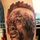 Life after formation: Veteran finds success in tattoo art A detailed realistic portrait tattoo on a person's leg/arm depicting a human face with dreadlocks and decorative head adornments. The tattoo uses a predominantly dark monochromatic palette with red accent shading. The work demonstrates high-level realism tattooing technique with fine detail in facial features and texture.