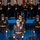Lt. Gen. Dana Kyle Chipman retirement ceremony A formal U.S. Army military ceremony is taking place on a stage with blue lighting. Several soldiers in dress uniforms are arranged in a precise formation, with a senior officer prominently positioned at the front center. A color guard holding flags is visible on a raised platform in the background.
